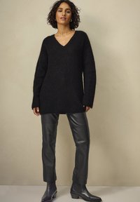 Sort langærmet sweater med V-hals, lavet af blødt, struktureret materiale, parret med tætsiddende sorte læderbukser og ankelstøvler.