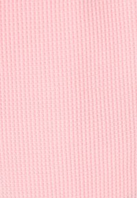 Rosa tyg med våffelmönster, som har ett rutmönster med upphöjda kanter, mjuk yta och enhetlig färgton genom hela textilen.