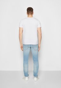 White short-sleeve t-shirt, light blue slim-fit jeans, and white sneakers. T-shirt has a round neckline; jeans feature back pockets and faded areas.