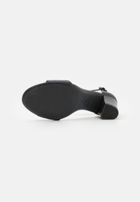 Sandale à talon en cuir noir vue par la semelle, montrant un talon bloc, une bride cheville et une indication de taille 37 en dessous.