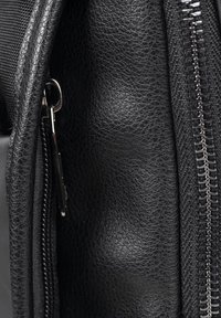 Sac en cuir noir avec surface texturée, doté d'une fermeture éclair latérale et de quincaillerie en métal. Les coutures détaillées ajoutent de l'intérêt visuel.