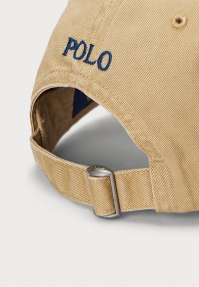 Béžová nastavitelná kšiltovka s kovovou sponou a tmavě modrým vyšitým nápisem "POLO" na zadním pásku.