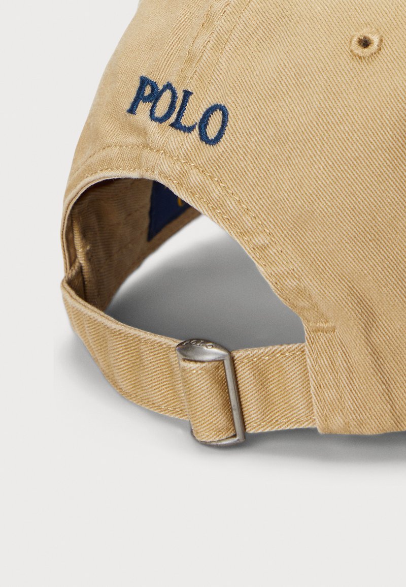 Beige verstelbare honkbalpet met metalen gesp en donkerblauwe "POLO" borduring op het achterste bandje.