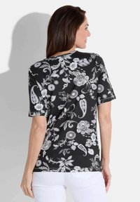 Haut noir à manches courtes avec un imprimé floral et paisley blanc, col rond et coupe décontractée. La vue arrière montre le motif et les détails du design.