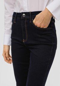 Donkerdenim jeans met een slank ontwerp, voorzien van contrasterende oranje stiksels, voorzakken en een metalen knoopsluiting.