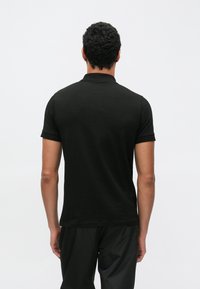 Črna polo majica s kratkimi rokavi, iz bombaža, z klasičnim ovratnikom in gladko teksturo. Hrbtni del ima prilagojeno silhueto.