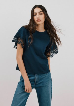 Navy blauwe t-shirt met kantafwerking op de mouwen, zachte katoenen stof, ronde halslijn, gecombineerd met lichtblauwe jeans, casual pasvorm.