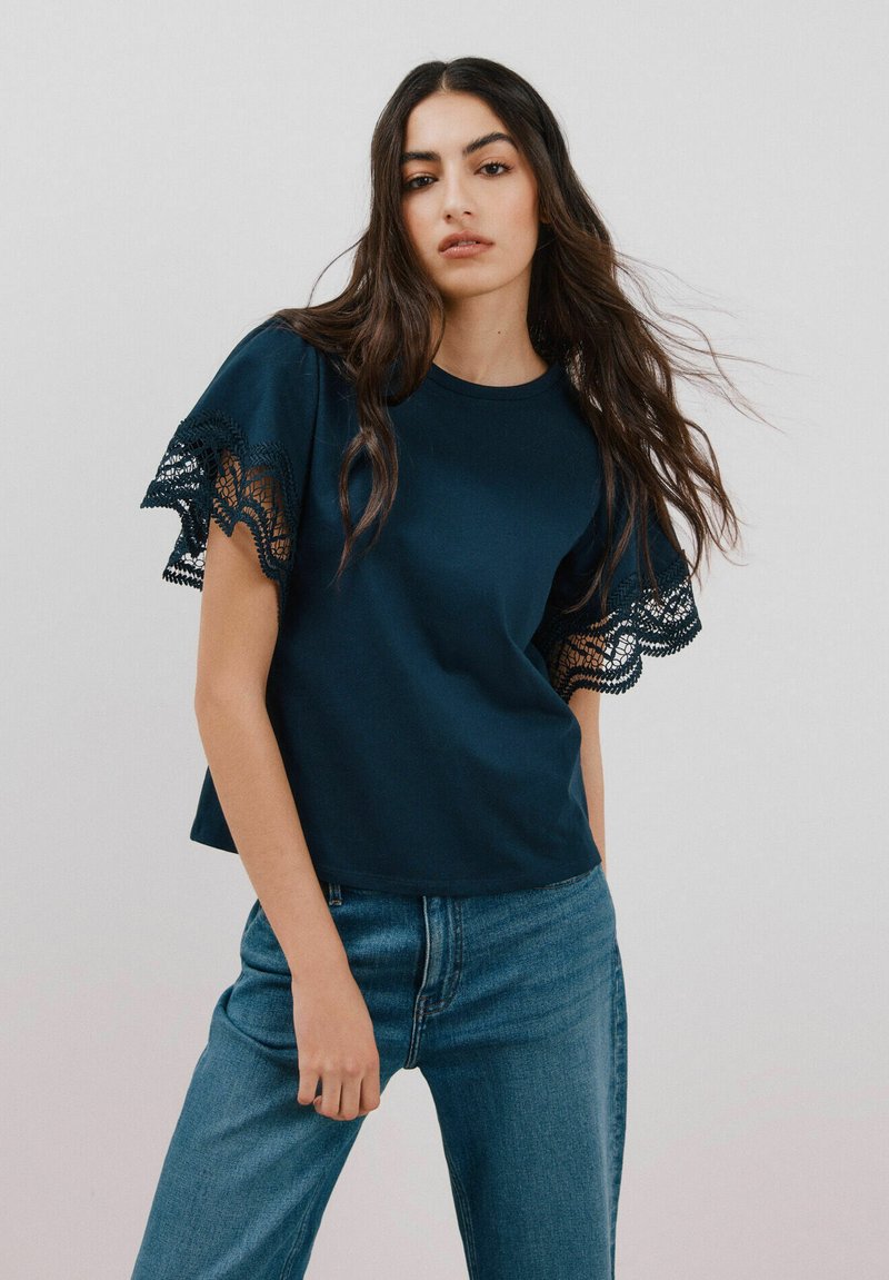 Navyblaue T-Shirt mit Spitzenbesatz an den Ärmeln, aus weichem Baumwollstoff, Rundhalsausschnitt, kombiniert mit hellblauen Jeans, lässige Passform.
