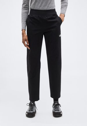 Pantalon noir à texture lisse, coupe fuselée et poches latérales. Doté d'un logo sur la cuisse droite. Associé à des chaussures de sport noires.