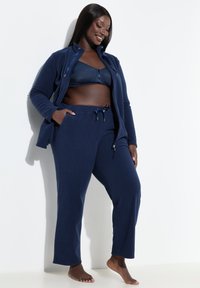 Marineblauwe fleecejas met een hoge kraag, ritssluiting en twee zakken, gecombineerd met bijpassende broek met een verstelbare tailleband met trekkoord.