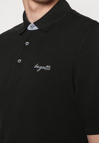 Polo shirt nera in cotone, con colletto classico rifinito in azzurro chiaro, tre bottoni e logo ricamato bianco.