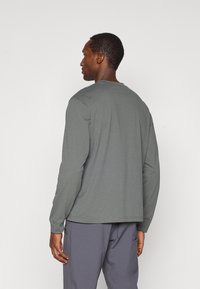 T-shirt de mangas longas em tecido cinza suave, com uma textura macia, apresentando um decote redondo e um corte descontraído, usado com calças cinzas claras.