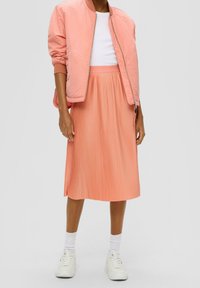 Chaqueta bomber rosa con puños acanalados sobre una camiseta blanca, combinada con una falda midi plisada rosa y zapatillas blancas. Texturas lisas, look casual.