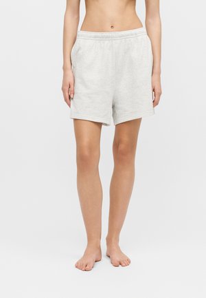 Woman wearing light gray elastic waist mid-thigh shorts, standing barefoot against plain background.