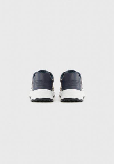 Un paio di sneakers blu navy con suole bianche viste da dietro su uno sfondo grigio chiaro semplice.