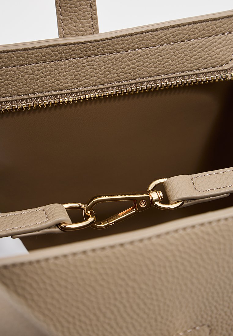 Beige leren tote bag interieur met een ritssluiting, voorzien van een gouden metalen sluiting en een gladde textuur.