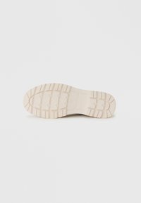 Suela de zapato color beige claro con superficie de goma texturizada y dibujo en la suela para un mejor agarre. Forma redondeada y bordes suaves.