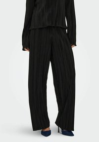 Ensemble noir plissé comprenant un haut ample et un pantalon à jambes larges, fabriqué dans un tissu doux avec une surface texturée. Agrémenté de talons aiguilles.
