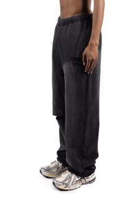 Črne široke hlače z vrvico v pasu, stranskimi žepi in gladkim teksturom, kombinirane s svetlimi športnimi copati.