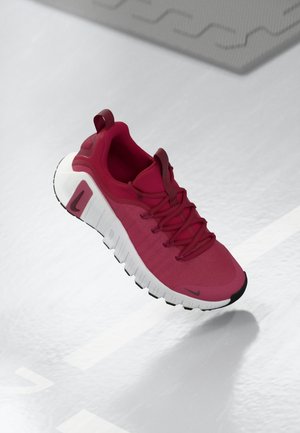 Chaussure de sport rouge avec semelle blanche segmentée et logo Nike noir, flottant au-dessus d'une surface texturée gris clair avec des ombres.