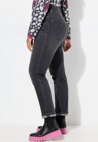 Jeans de denim gris oscuro con un ajuste slim, puños enrollados, bolsillos traseros, combinados con botas de tobillo negras que tienen una suela rosa sobredimensionada.