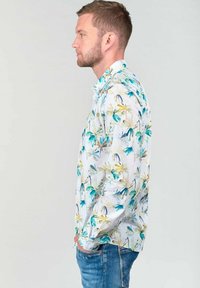 Witte langermige shirt met een veelkleurig bloemenpatroon in groen, blauw en geel. De stof lijkt zacht en heeft een ontspannen pasvorm.