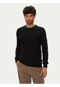 Marineblauer gestrickter Pullover mit strukturiertem Zopfmuster, rundem Ausschnitt und gerippten Bündchen; wird mit beigen Hosen getragen und besitzt ein Logo-Detail am Saum.