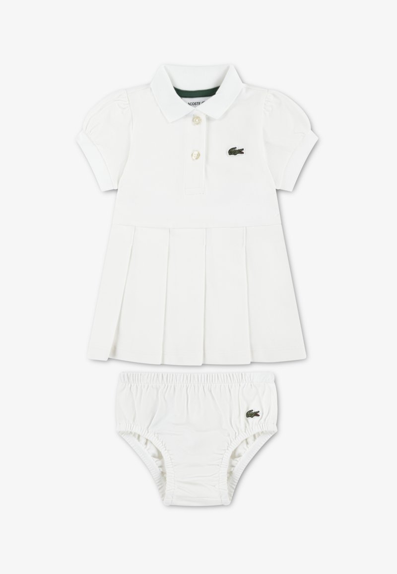 Λευκό βαμβακερό φόρεμα με γιακά πόλο, φουσκωτά μανίκια και πλισέ φούστα. Περιλαμβάνει λευκά σορτς με ελαστική μέση και λογότυπο που ταιριάζουν.