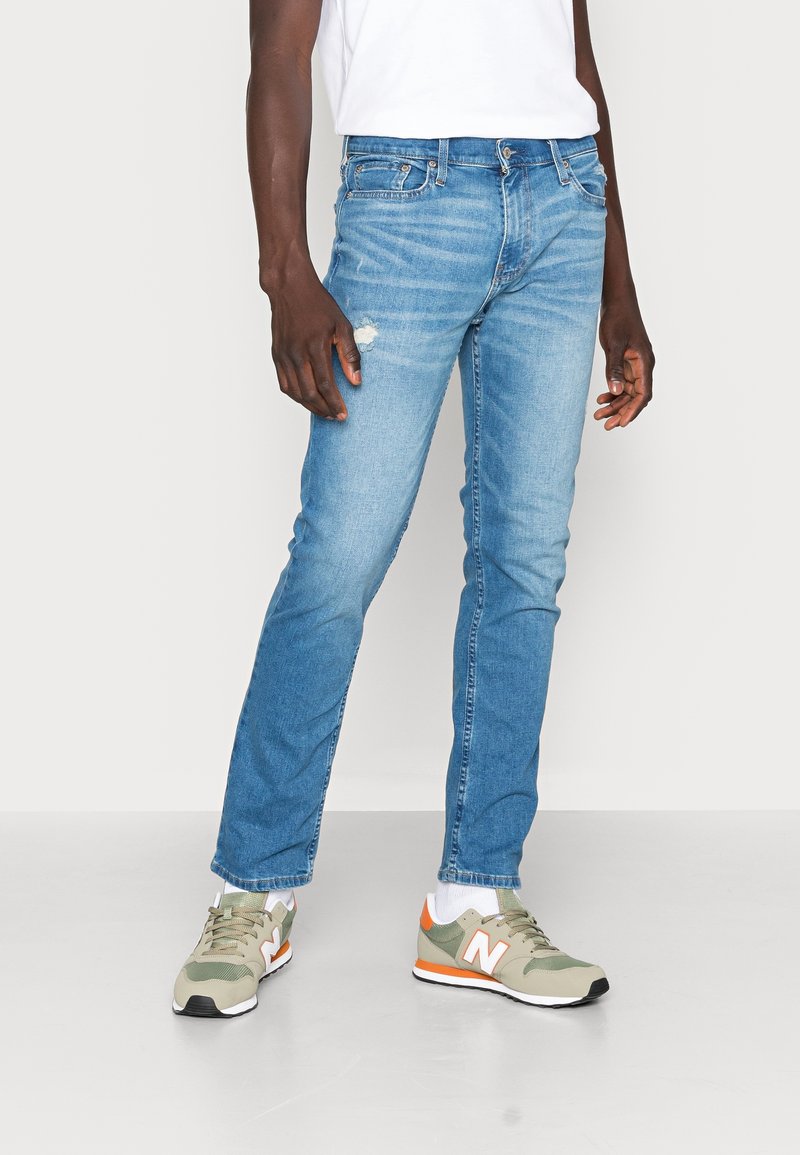 Ljusblå denimjeans med slim fit, med en slitning på låret. Kombineras med gröna och orange sneakers.