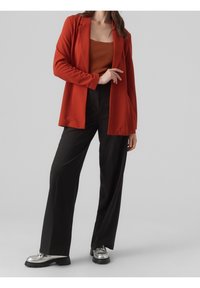 Röd kavaj med en avslappnad passform, bärs över en orange ribbad linne. Svarta vida byxor och klumpiga silverfärgade skor fulländar outfiten.