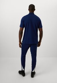 Mørkeblå polo-shirt og bukser lavet af glat materiale, med en klassisk krave og sidelommer med lynlås på bukserne. Enkel design uden mønstre.