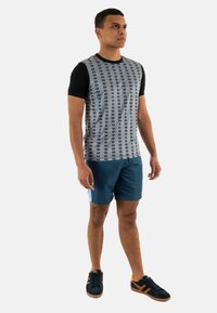 Camisa de hombre de manga corta en negro y gris, con rayas verticales y un patrón gráfico repetido; combinada con pantalones cortos azules y zapatillas náuticas.