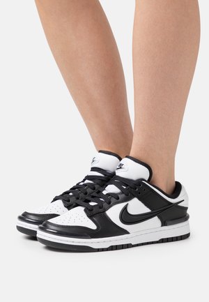 Sneaker Nike in bianco e nero con tomaia in pelle, punta forata e suola ammortizzata, caratterizzati dal logo swoosh nero sul lato.