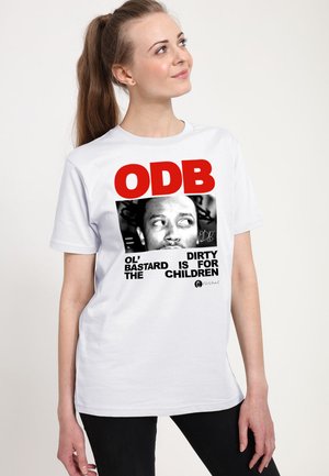 Ung kvinde med langt hår sat op i hestehale iført en hvid t-shirt med ODB-tekst og et sort-hvidt portrætgrafik.