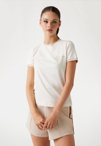 Crème T-shirt met korte mouwen, gemaakt van zachte katoen, met een subtiele logo op de borst en een ronde halslijn. Gecombineerd met lichte shorts.