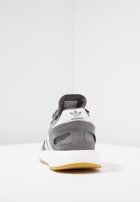 Grå mockainsko med vita accenter, med en texturerad ovandel, ventilerande mesh och en dämpad gummisula. Adidas-logotyp synlig.