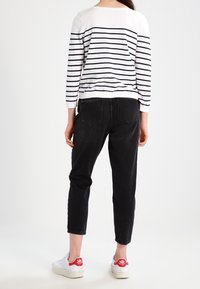 Gestreepte witte en marineblauwe trui, zwarte cropped jeans en witte sneakers met rode accenten. Glad textuur en casual ontwerp.