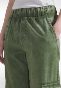 Grønne, lette bukser med elastik i taljen, sidelommer og en afslappet pasform. Stoffet har en blød tekstur med en subtil glans.