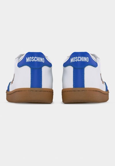 Λευκά αθλητικά παπούτσια με μπλε ταμπελάκια στη φτέρνα και καφέ σόλες, με την επιγραφή "MOSCHINO" σε λευκό πάνω στα μπλε ταμπελάκια της φτέρνας, εμφανιζόμενα από πίσω.