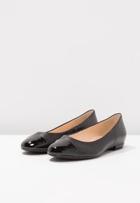 Ballerine in pelle nera con punta a cappuccio in vernice nera lucida e finitura opaca. Forma arrotondata, tacco basso e interno liscio.