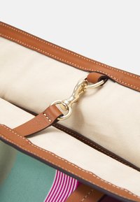 Brown leather bag interior featuring a gold metal clip, tan fabric lining, and contrasting colorful patterns on the exterior.