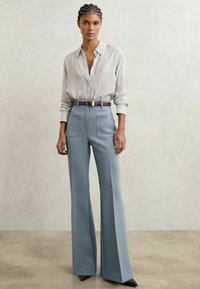 Kergelt triibuline nööbitav särk, mis on kombineeritud kõrge vöökohaga laia säärega siniste pükstega, millel on pruuni vöö kuldse pandlaga.