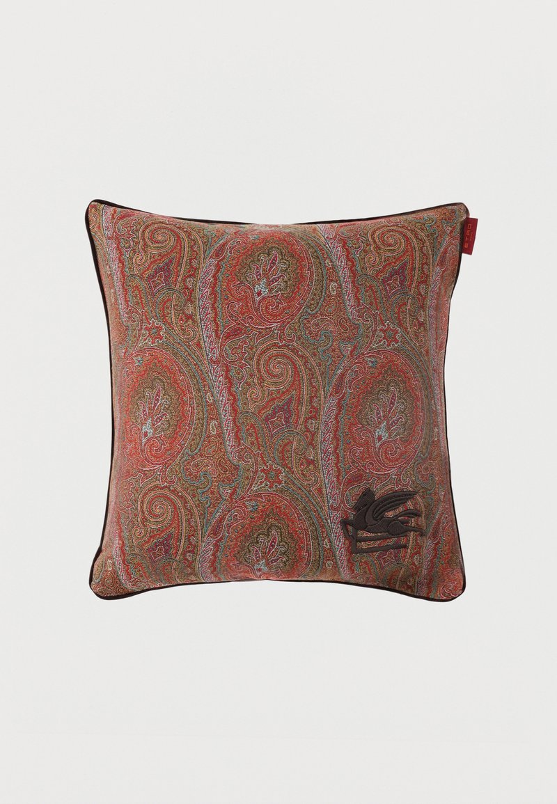 Coussin carré décoratif avec un motif cachemire complexe en rouge, marron et bleu, et un petit emblème d'oiseau brodé en bas à droite.