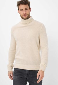 Maglione beige a collo alto realizzato in tessuto morbido e strutturato. Presenta maniche lunghe e dettagli a coste sui polsini e sull'orlo.