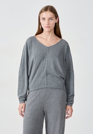 Grauer V-Ausschnitt-Pullover mit langenÄrmeln, weichem Material, lockerer Passform und gestepptem Nahtdetail an der Vorderseite. Kombiniert mit passenden gerippten Hosen.