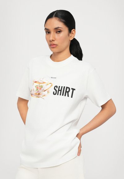 T-shirt alb din bumbac, cu un grafic colorat al unei cești de ceai și cuvântul "SHIRT" în litere negre îngroșate pe față. Mâneci scurte, guler rotund.