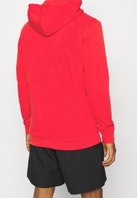 Roter Pullover-Hoodie aus weichem Stoff, mit Kapuze und gerippten Bündchen, kombiniert mit schwarzen Shorts. Fokussiert auf Einfachheit und Komfort.
