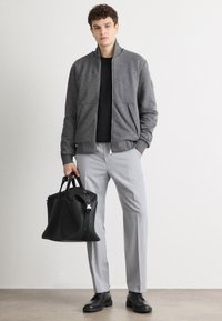 Giacca bomber grigia con zip frontale, due tasche e polsini a costine. Abbinata a pantaloni grigi chiari e una borsa a tracolla in pelle nera. Scarpe nere.