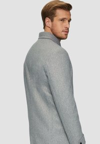 Lichtgrijze wollen coat met een op maat gemaakte ontwerp, inkeping kraag en knoopaccenten. Gladde textuur met subtiele spikkeldetails.