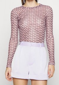 Blusa de manga larga y transparente con un patrón geométrico en rosa y negro, combinada con pantalones cortos de talle alto en lavanda con dobladillos doblados.